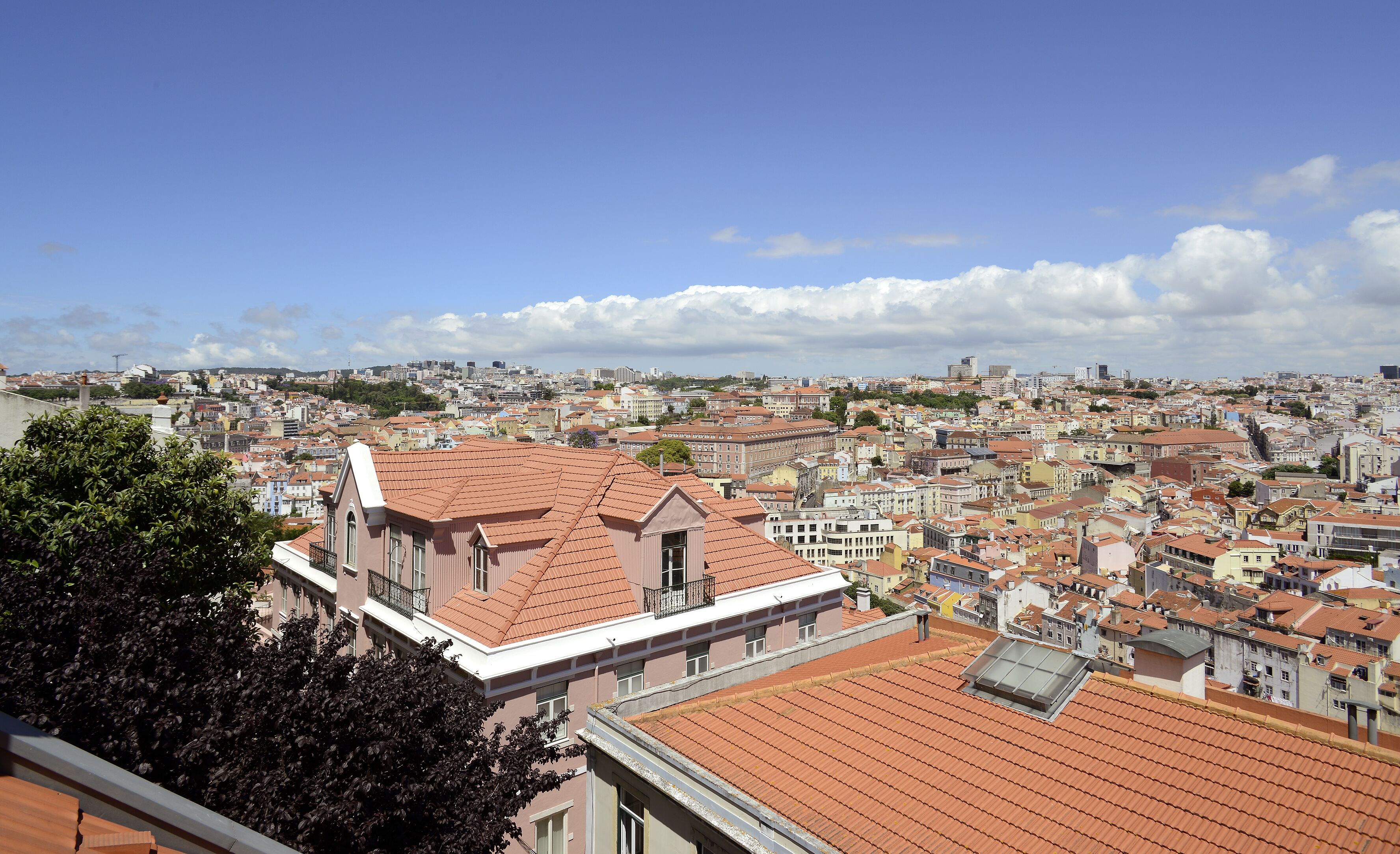 A cityscape with a prominent building featuring a red-tiled roof and a balcony.