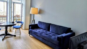 Una sala de estar moderna con un sofá azul, una mesa roja, una lámpara y un televisor.