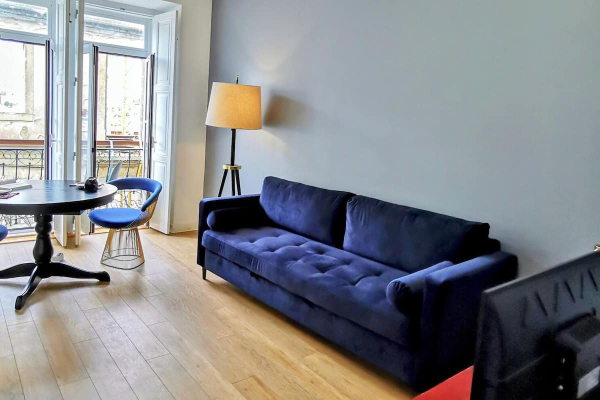 Una sala de estar moderna con un sofá azul, una mesa roja, una lámpara y un televisor.