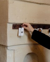 Una mano sostiene una etiqueta con el texto "PALAZZO DEL DUCA HOTEL & RESTAURANT" adherida a una pared.