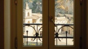 Una vista attraverso una porta con cancello in metallo, che mostra un paesaggio montuoso con edifici e una chiesa.