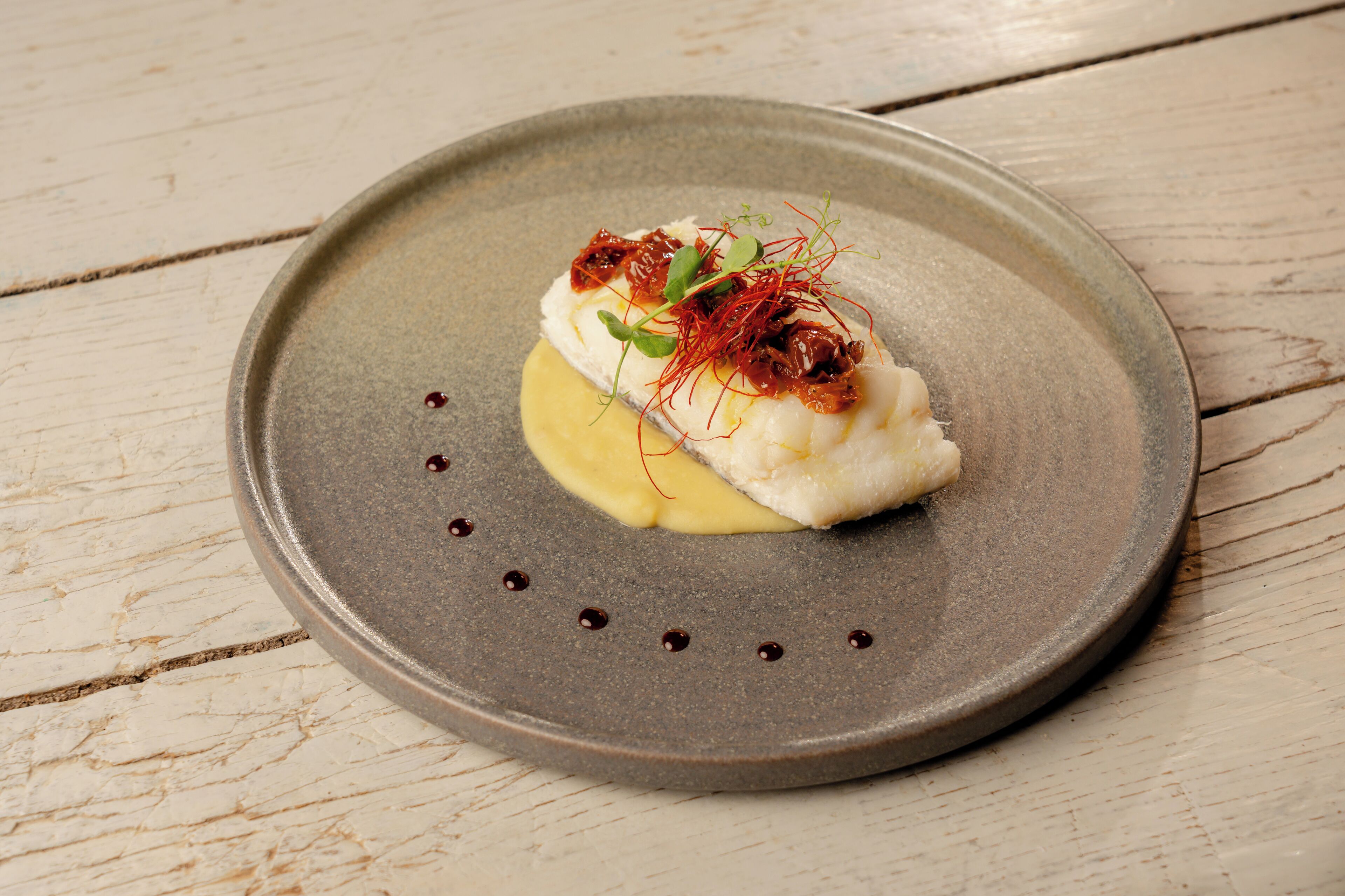 A dish with a white base, garnished with red elements and green leaves, served on a round, speckled plate.