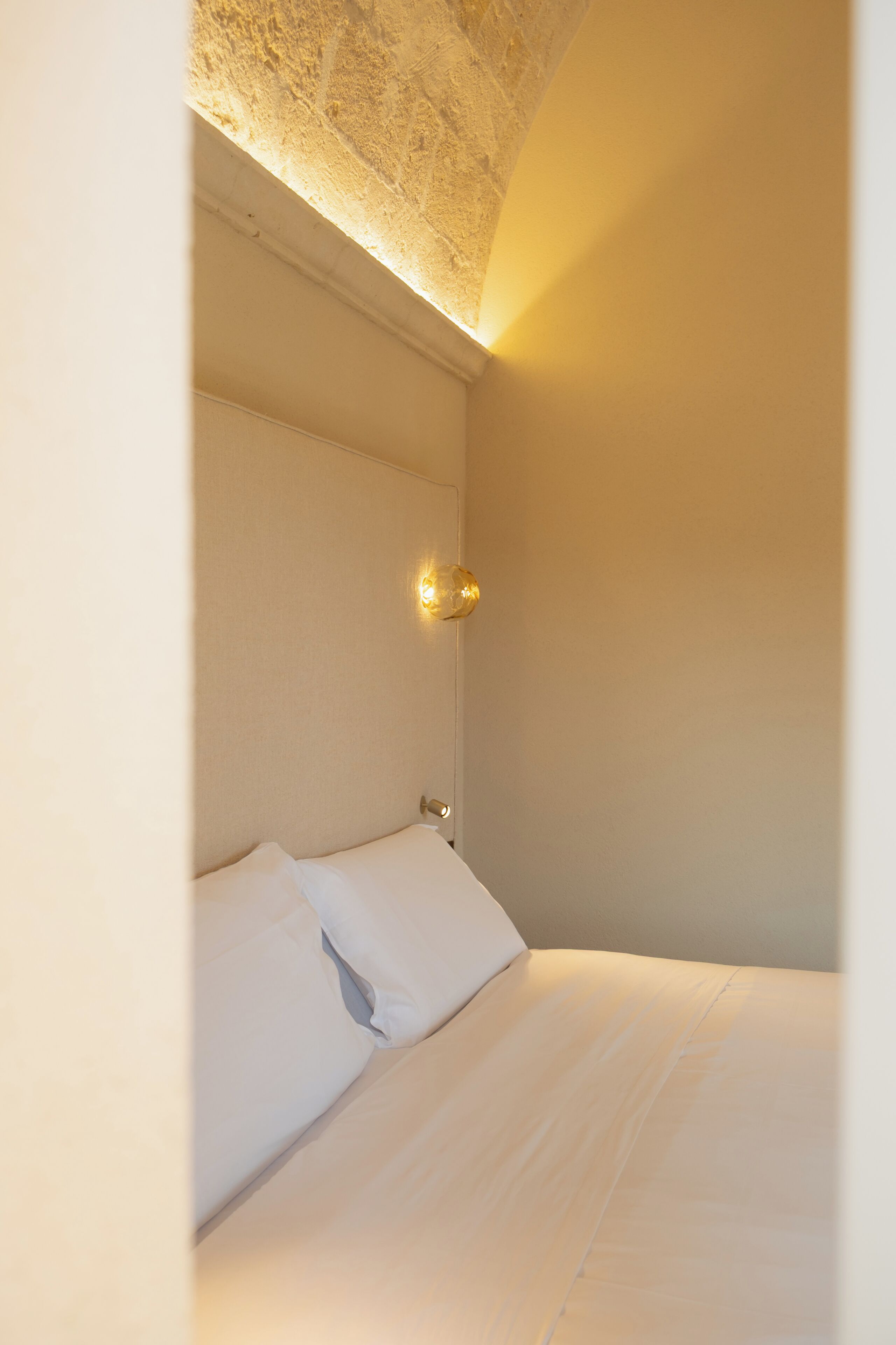 Un letto rifatto con lenzuola bianche in una stanza con soffitto strutturato e un punto luce a parete.