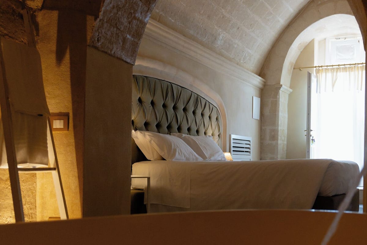 A bedroom with a bed under an arched ceiling, a headboard with a tufted design, and a window with curtains.