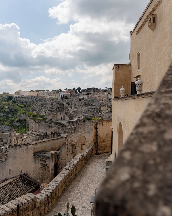Un edificio histórico de piedra con un patio, con vistas a una zona urbana densamente poblada con arquitectura tradicional y una ladera rocosa.