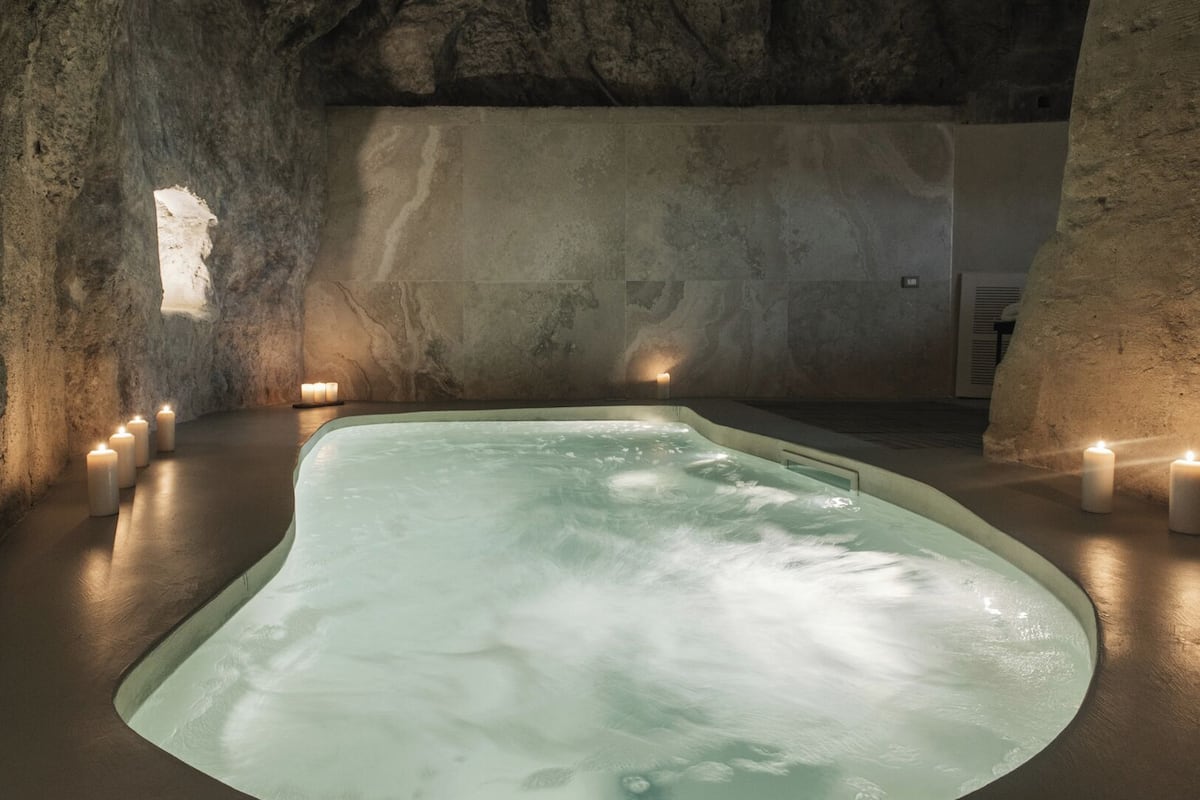A spa area with a hot tub surrounded by candles, set against a stone wall.