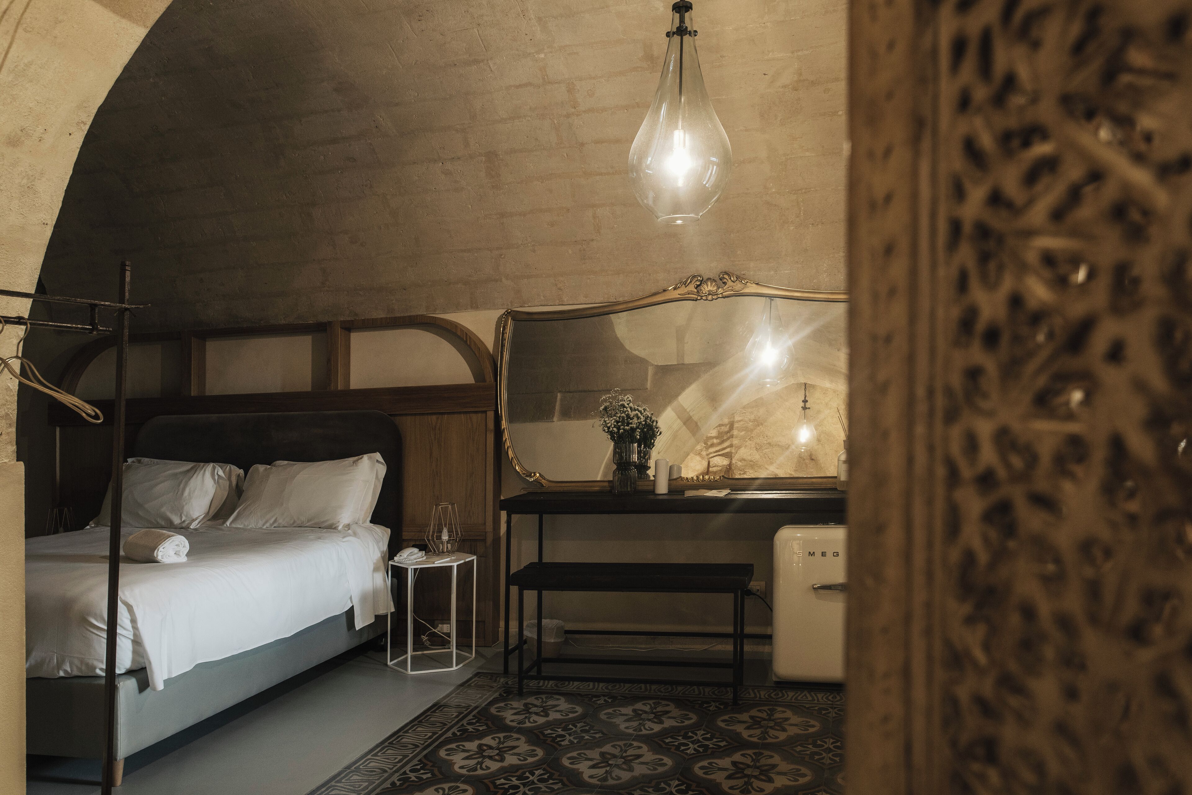 A bedroom with a bed, bedside table, and a desk with a mirror.