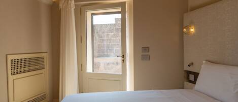 A hotel room with a bed, a window with curtains, a radiator, and a wall-mounted light fixture.