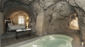 Una stanza spa con parete in pietra, un letto, un tavolo con asciugamani e una vasca idromassaggio.