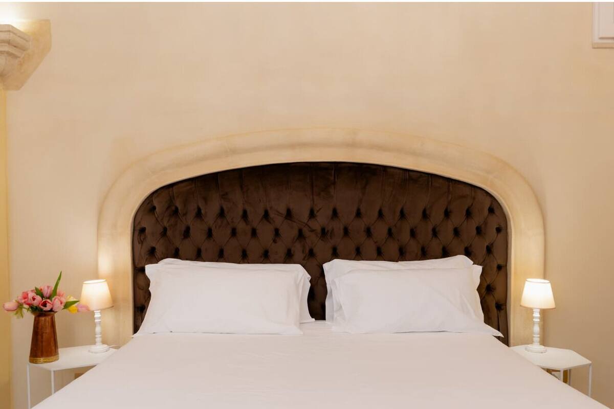 A neatly made bed with a tufted headboard, two white pillows, and two bedside lamps on white nightstands.