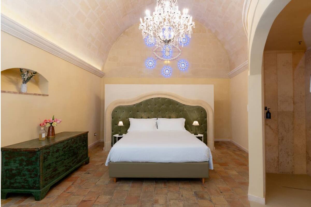 A bedroom with a large bed, a chandelier, a nightstand, and a dresser.