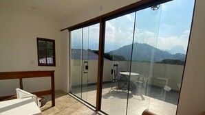 Una habitación moderna con un amplio ventanal corredero que da a un balcón con vistas a montañas.
