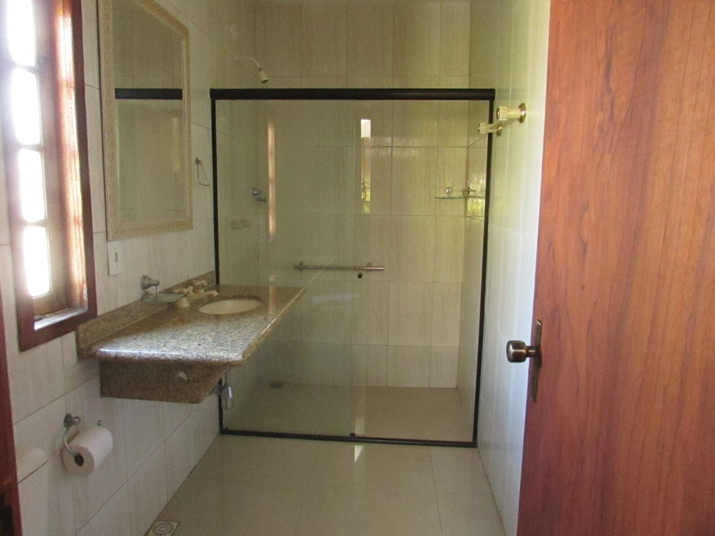 A bathroom with a glass shower door, a sink with a marble countertop, and a toilet paper holder.