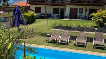 Um hotel com piscina, espreguiçadeiras e um edifício de dois andares.