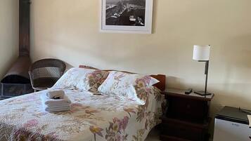 Habitación de hotel con cama, una silla, escritorio, lámpara y refrigerador.