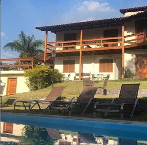 A two-story building with a balcony, a swimming pool, and outdoor seating. - Pousada Village Terê (Teresópolis)