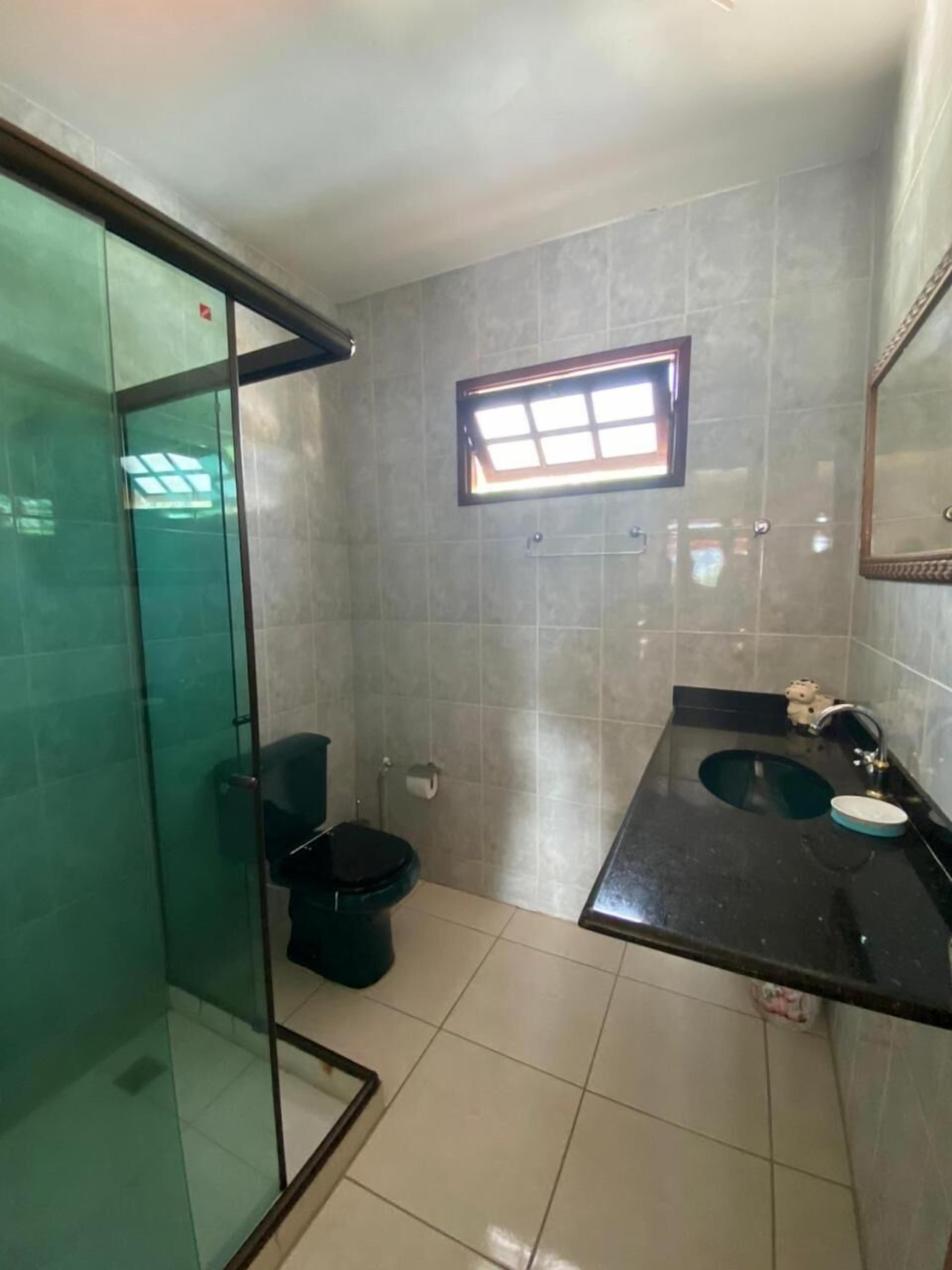 A bathroom with a glass shower enclosure, a toilet, a sink with a mirror, and a window providing natural light.