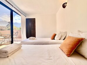 A hotel room with two beds, a balcony with a table and chairs, and a mountain view. - La Bergerie (Ouirgane)