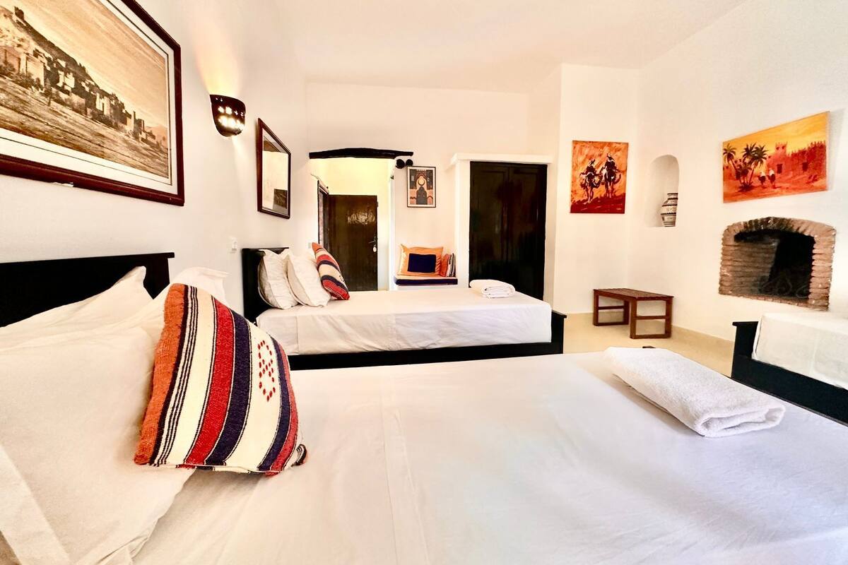 Une chambre d’hôtel avec deux lits, une cheminée et des œuvres d’art aux murs.