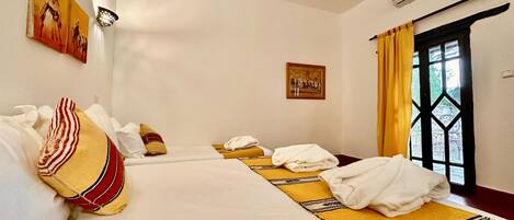 A hotel room with two beds, a window with curtains, an air conditioning unit, and artwork on the walls.