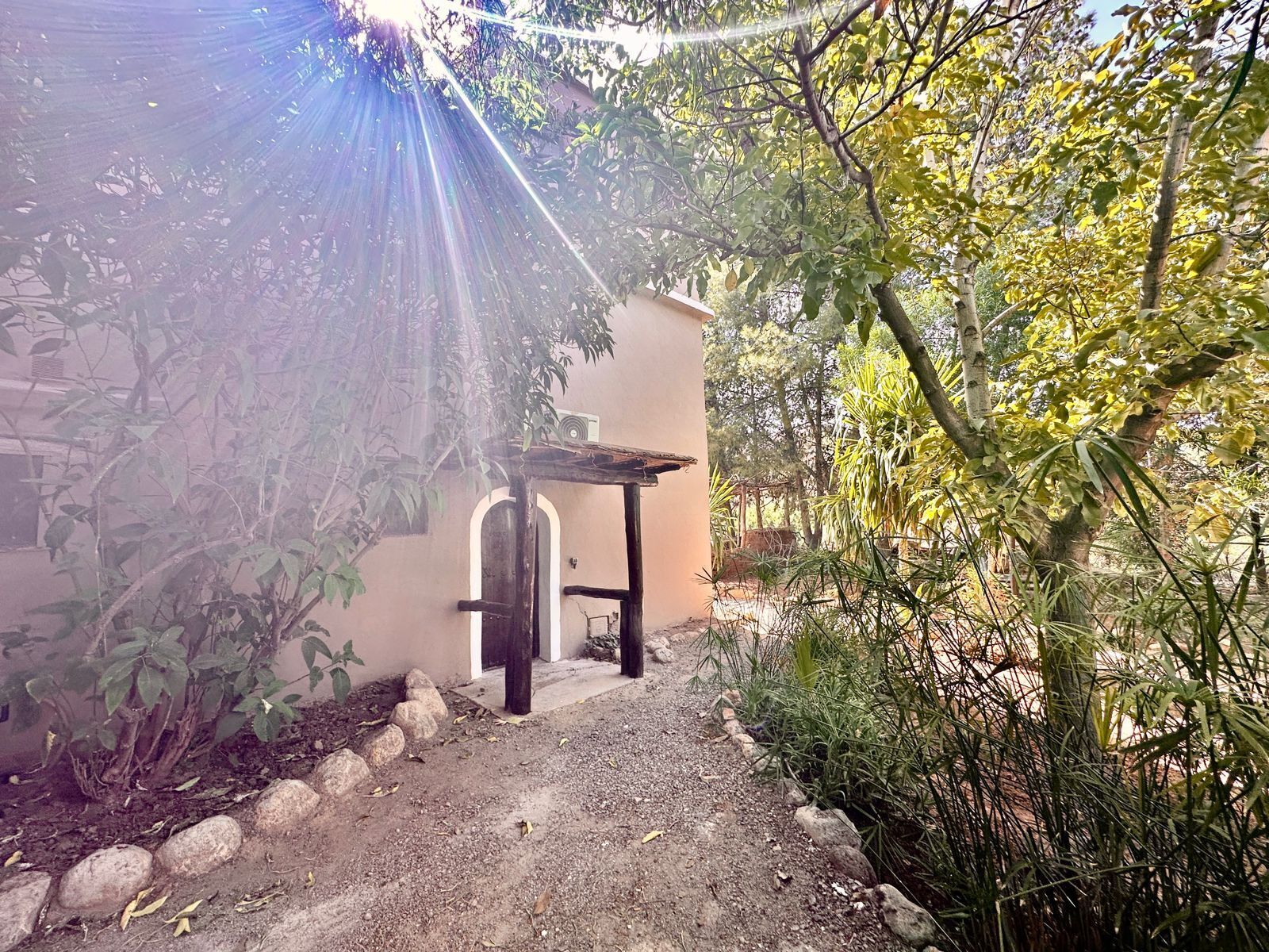 Un sendero conduce a un edificio con una zona exterior cubierta, rodeado de vegetación y rocas.