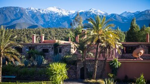 A stone building with a red roof, surrounded by palm trees and a mountainous backdrop. - La Bergerie (Ouirgane)