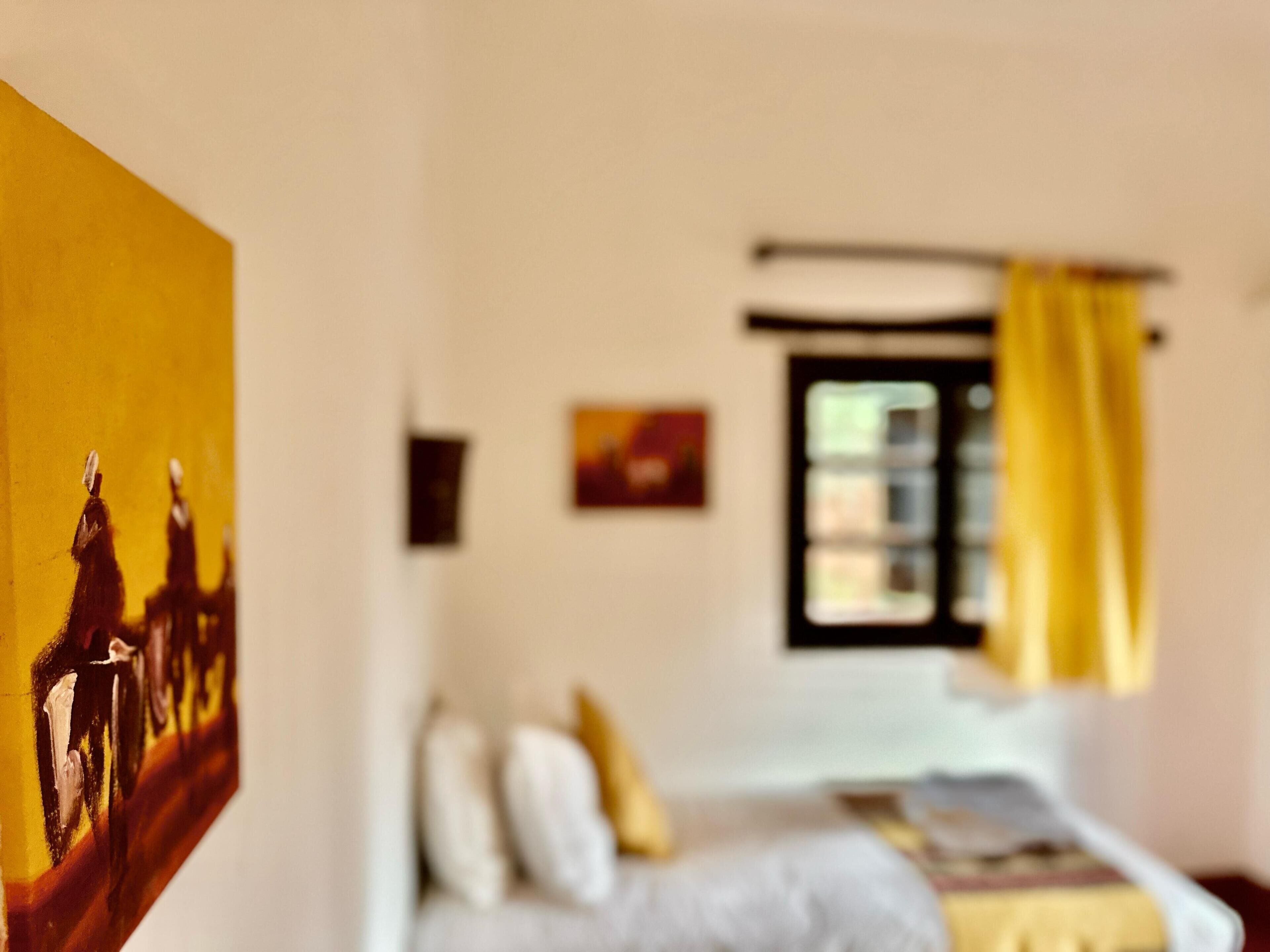A room with a bed, a window with yellow curtains, and a painting on the wall.