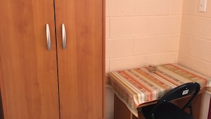 A small room with wooden wardrobes, a small table with a patterned tablecloth, and a black chair. - Hostal Vilama (San Pedro de Atacama)