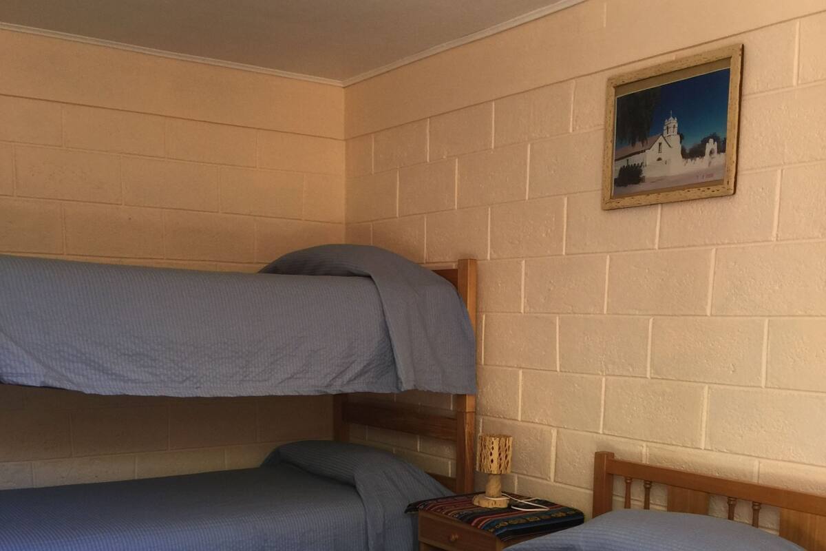 A room with two bunk beds, a small bedside table with a lamp, and a framed picture on the wall.