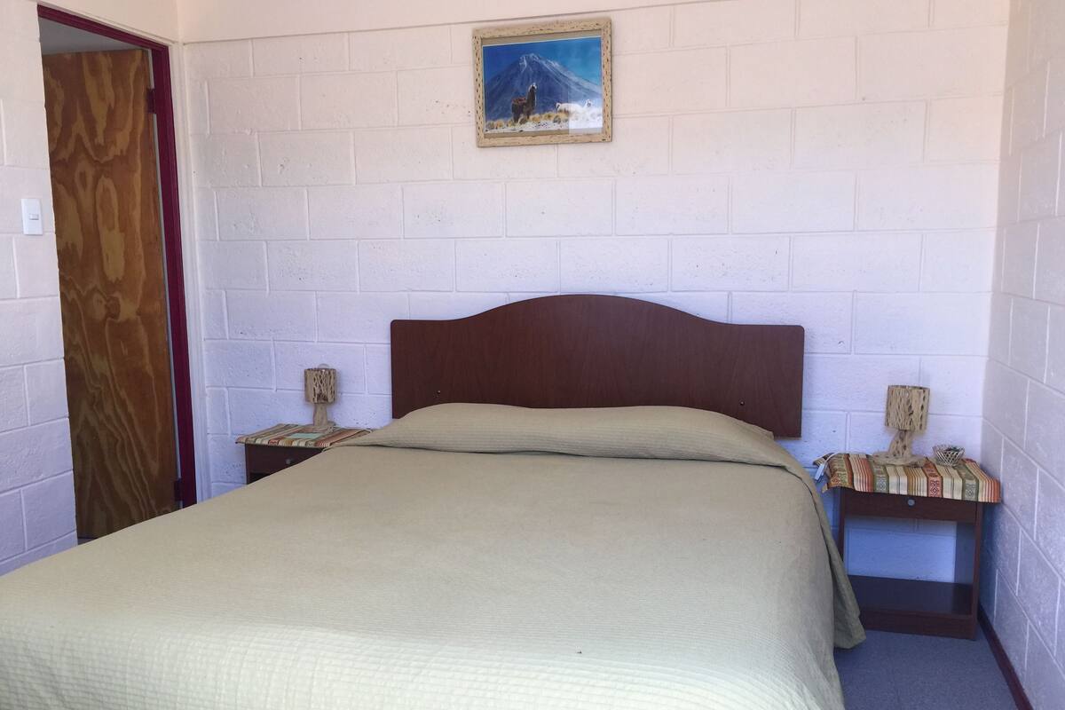 A single bed with a wooden headboard in a room with white brick walls. There is a framed picture on the wall above the bed.