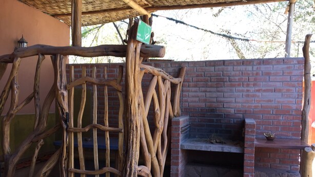 A rustic outdoor seating area with a brick fireplace, wooden railings, and a sign indicating a functional space. - Hostal Vilama (San Pedro de Atacama)
