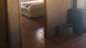Una habitación rústica con una cama, una chimenea y vistas a otro dormitorio por un umbral abierto.