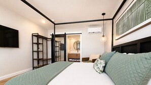 A bedroom with a bed, a TV mounted on the wall, a wardrobe, and a bathroom visible through an open door. - Bali Hai Resort, a Dazzler Select by Wyndham (Atlantic Beach)
