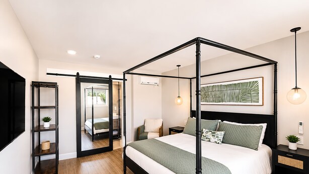 A four-poster bed with a white and green bedspread, a black metal frame, and a bedside table with a lamp. - Bali Hai Resort, a Dazzler Select by Wyndham (Atlantic Beach)