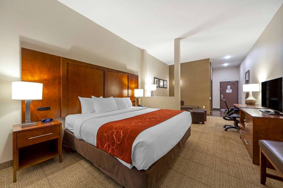Ein Hotelzimmer mit einem großen Bett, Nachttischen, einem Schreibtisch mit Stuhl, einem Fernseher und einem Spiegel.