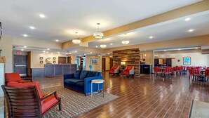Un hall d’entrée spacieux, avec un canapé bleu, des fauteuils rouges et un comptoir d’accueil en bois.
