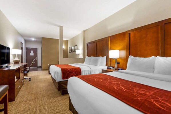 Habitación de hotel con dos camas, un escritorio, una silla, un televisor y una lámpara.