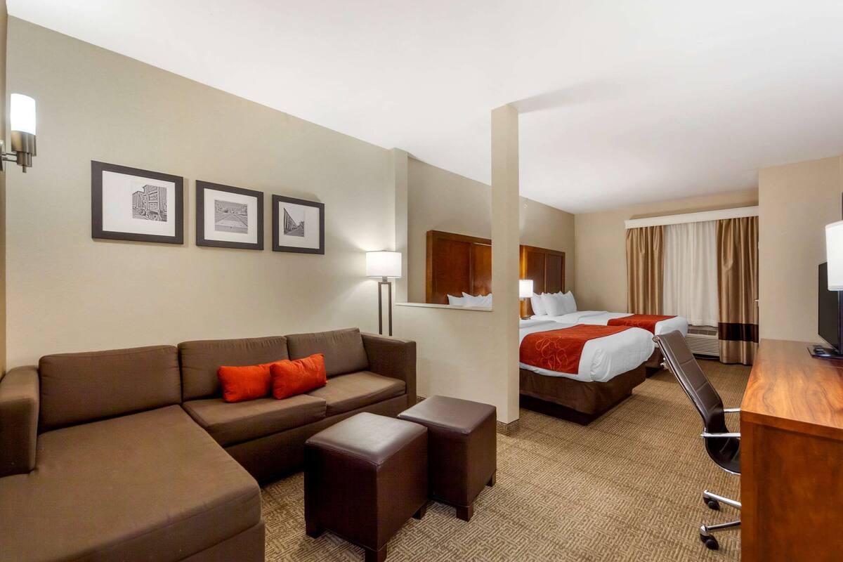 Ein Hotelzimmer mit einer Couch, zwei Betten, einem Schreibtisch und gerahmten Bildern an der Wand.