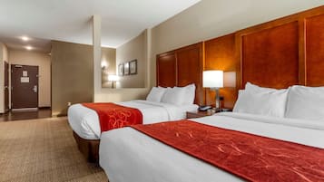 Habitación de hotel con dos camas, cabecero de madera, piso alfombrado y una mesita de noche con lámpara.