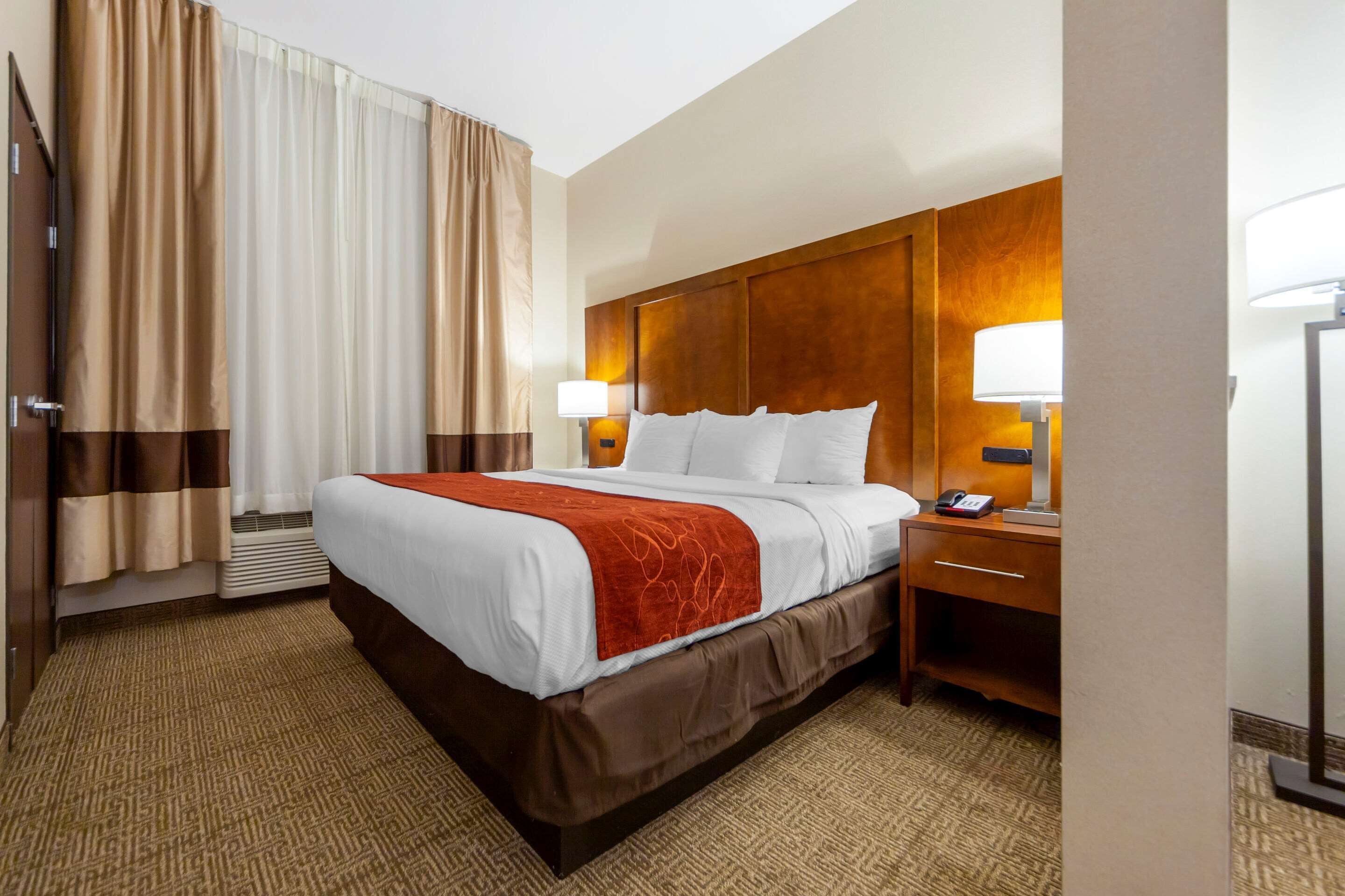 Una habitación de hotel con una cama grande, dos mesitas de noche con lámparas, un cabecero de madera y piso alfombrado.