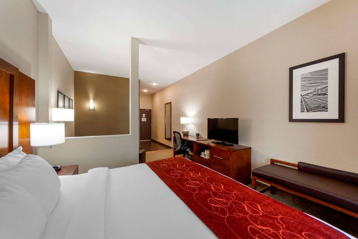 Ein Hotelzimmer mit Bett, Fernseher, Schreibtisch, Stuhl, Lampe, Spiegel und einem gerahmten Bild an der Wand.