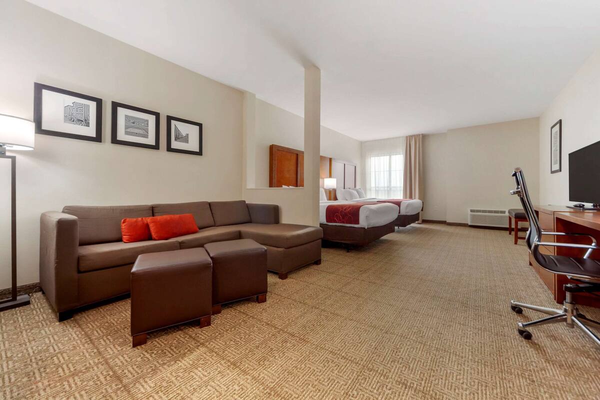 Ein Hotelzimmer mit Ecksofa, Schreibtisch, Bett und gerahmten Bildern an der Wand.