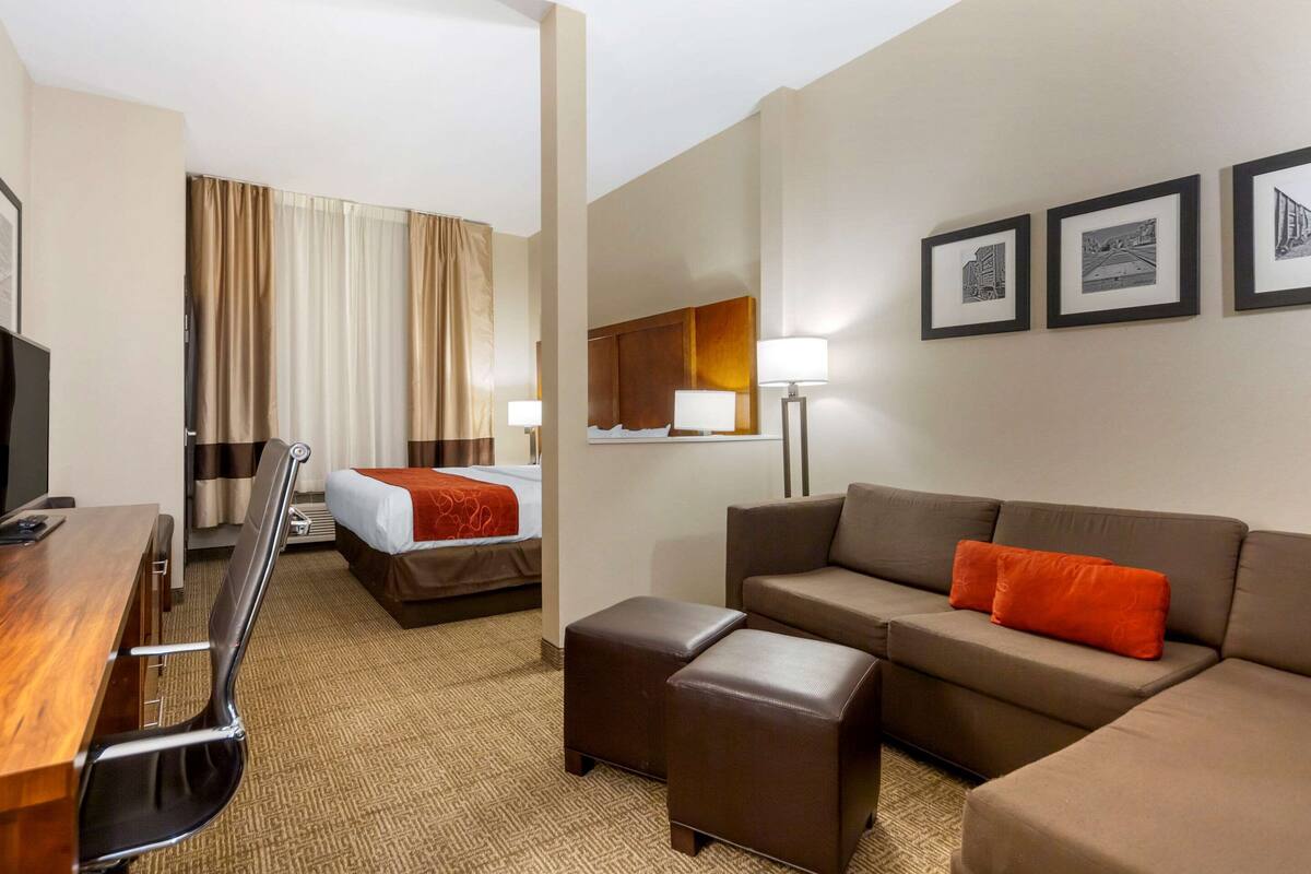 Ein Hotelzimmer mit Bett, Sofa, Schreibtisch und Stuhl. An der Wand hängen drei gerahmte Bilder.