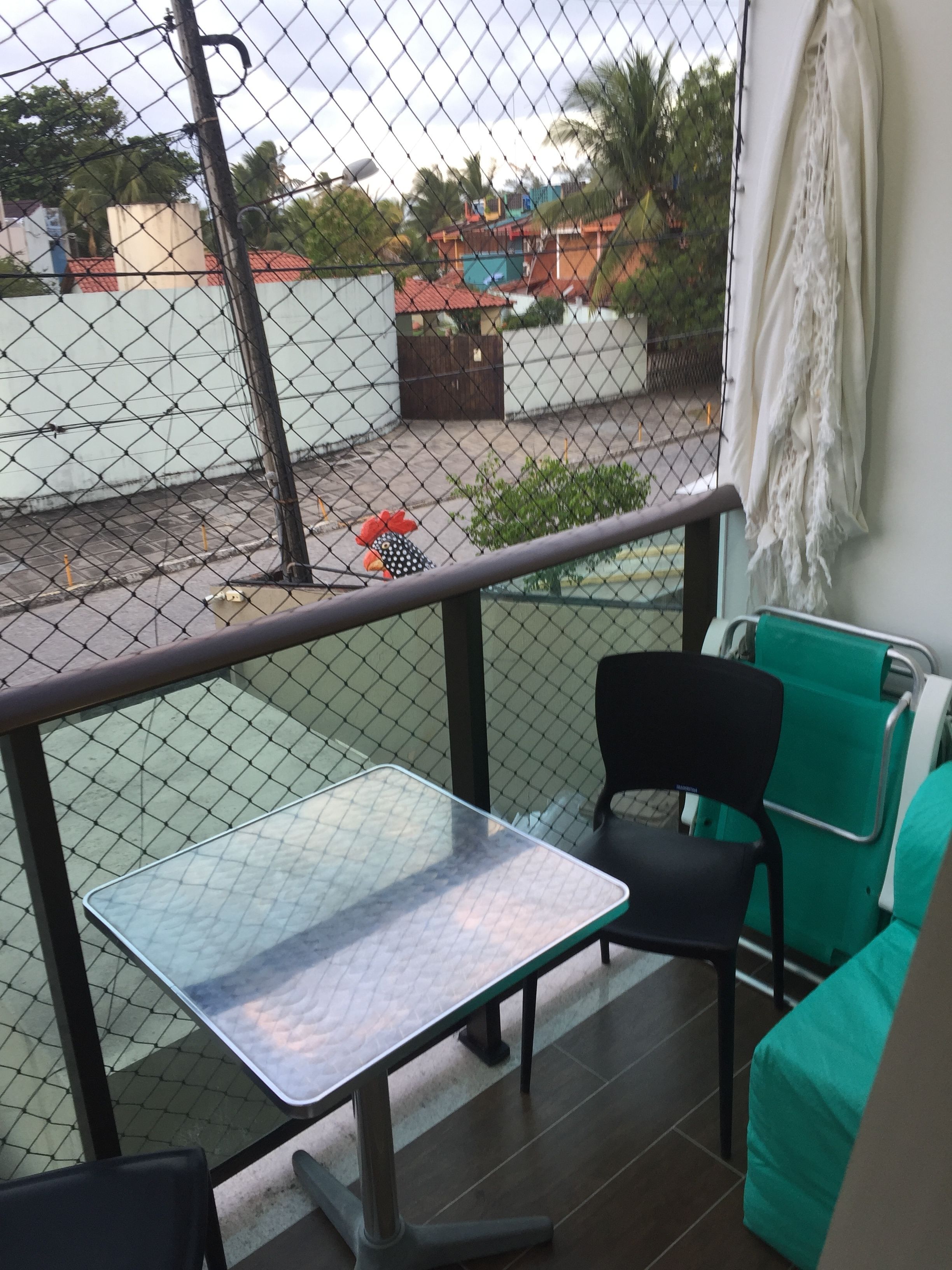 Uma varanda com uma mesa de metal e duas cadeiras, uma verde e outra preta.
