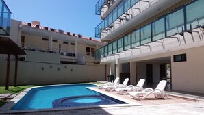 Un edificio moderno con piscina, sillones de descanso y fachada de vidrio.