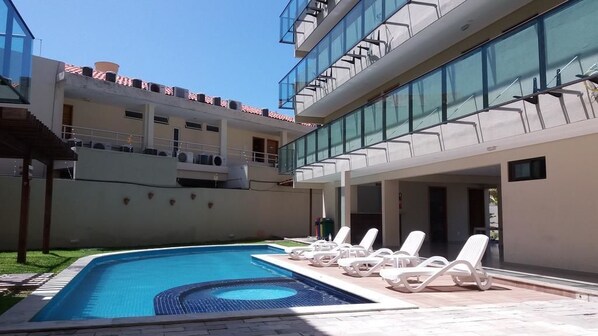 Un bâtiment moderne doté d’une piscine, de chaises longues et d’une façade en verre.