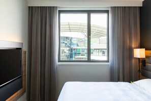 Une chambre d’hôtel avec un lit, une télévision, une fenêtre avec des rideaux et une lampe.