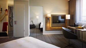 Een moderne hotelkamer met een groot bed, een bureau met lamp, een televisie en een gitaar op de achtergrond.