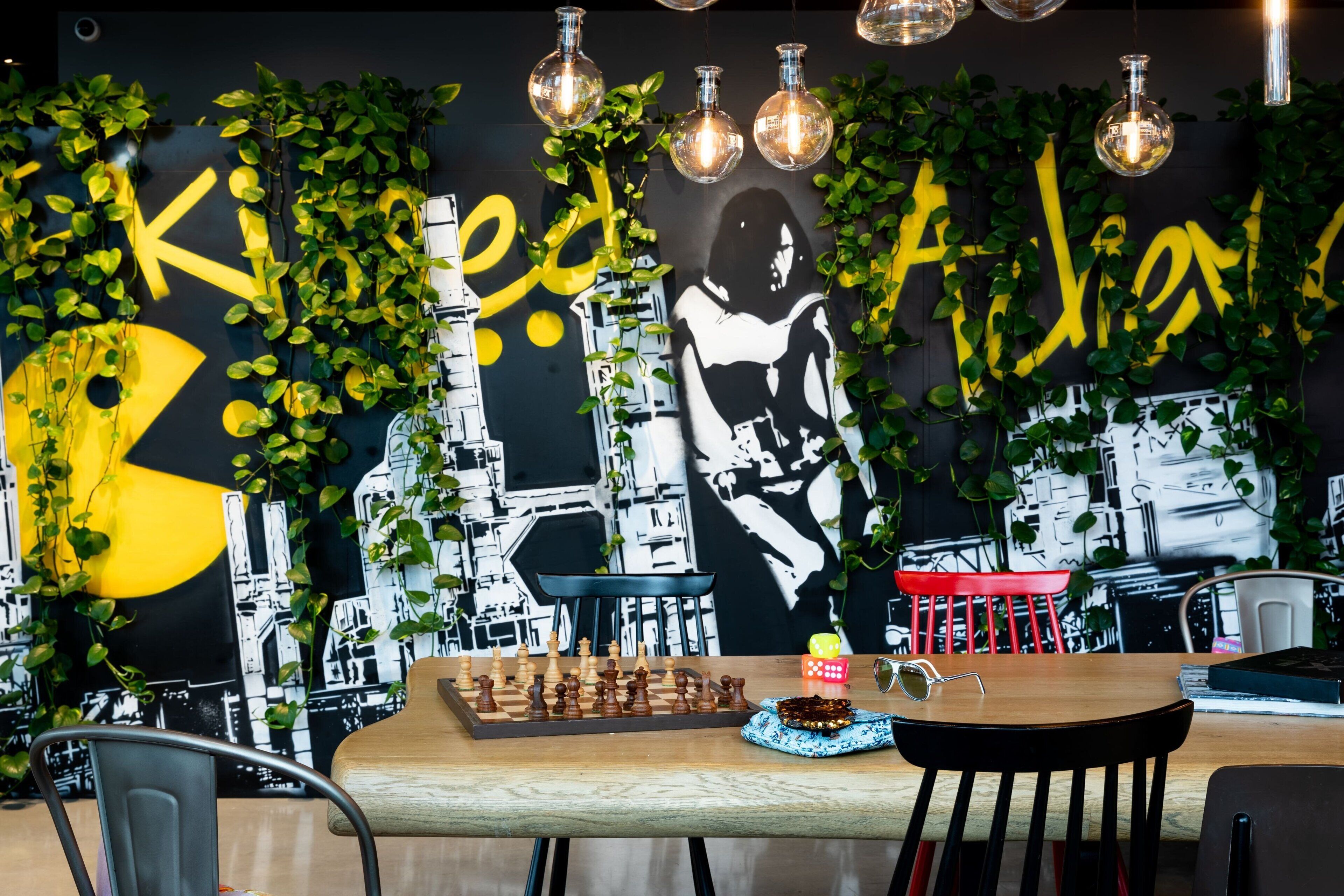 Un intérieur moderne avec un jeu d’échecs, une table avec une bougie et un mur orné de graffitis et de plantes.