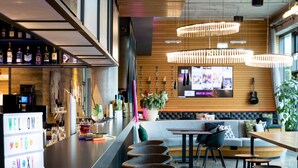 Een moderne bar met een lange toonbank, meerdere barkrukken en een televisiescherm waarop een menu wordt getoond.